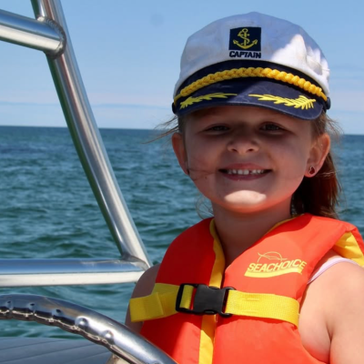 Young Captain Enjoying a Family Boat Adventure on Cape Cod Young girl wearing a captain's hat and life jacket while smiling aboard a boat on Cape Cod Bay during a family boating adventure