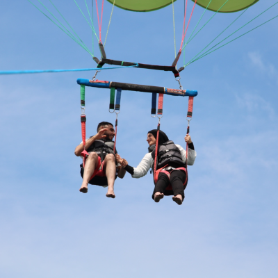 Couples Parasailing Over Cape Cod Bay | Dennis Parasail & Jet Ski Couple parasailing high above Cape Cod Bay, holding hands and enjoying scenic ocean views during a tandem parasail flight with Dennis Parasail & Jet Ski.