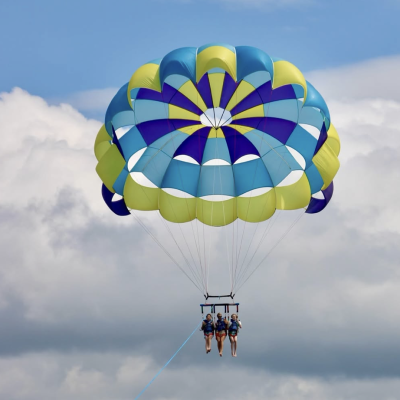 Triple Parasailing Adventure Over Cape Cod Bay Three people parasailing over Cape Cod Bay with Dennis Parasail & Jet Ski, soaring high above the water under a colorful parasail.