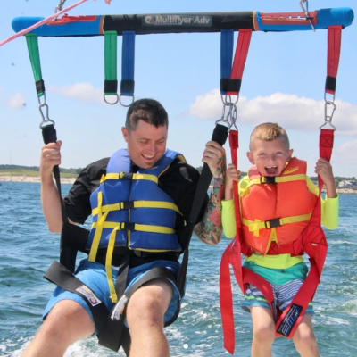 Father & Son Parasailing Adventure Over Cape Cod Bay Father and son parasailing together over Cape Cod Bay, smiling and enjoying a family-friendly adventure above the water with Dennis Parasail & Jet Ski.